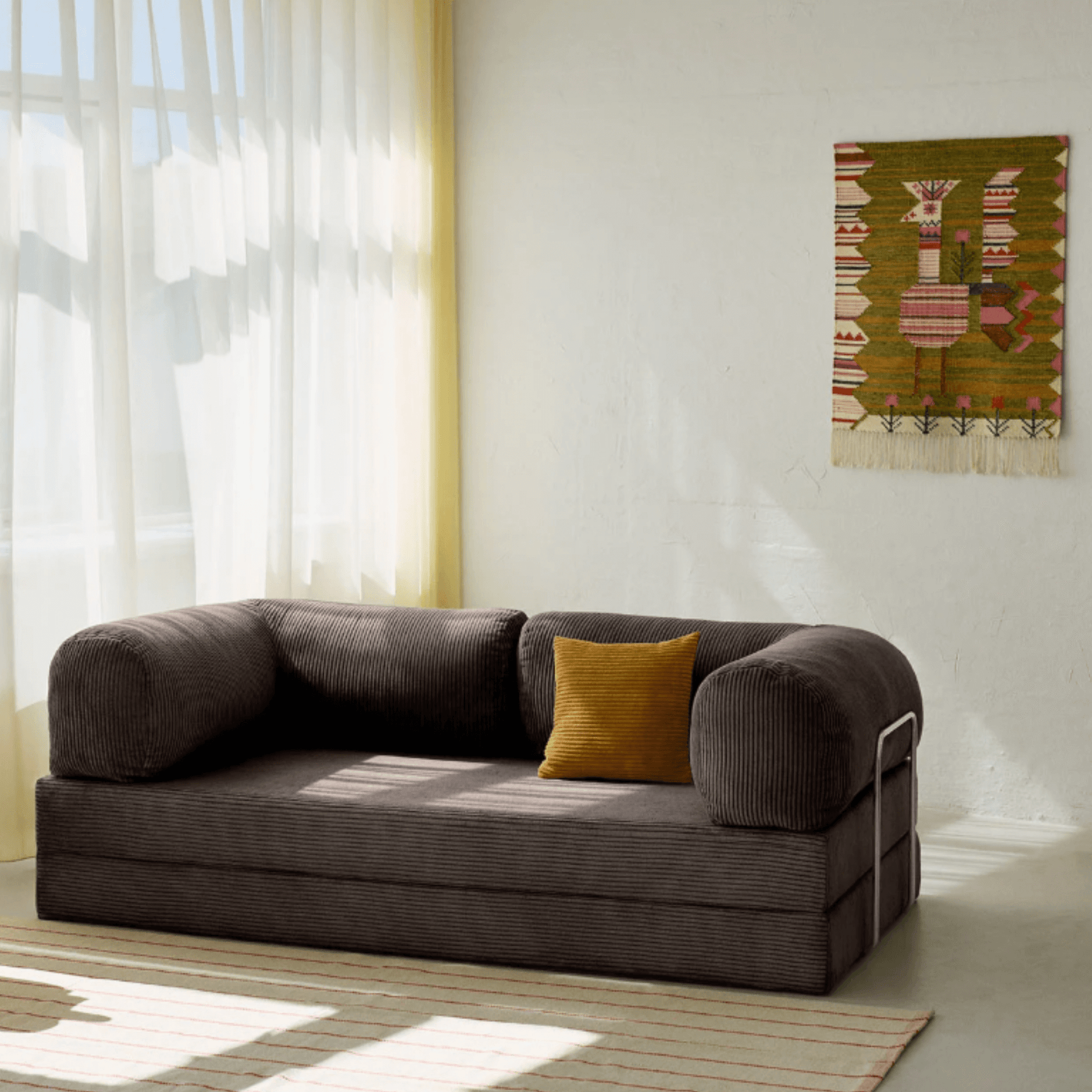 Primyhome coffee brown corduroy convertible sofa bed in a sunlit living room with minimalist decor and boho wall art