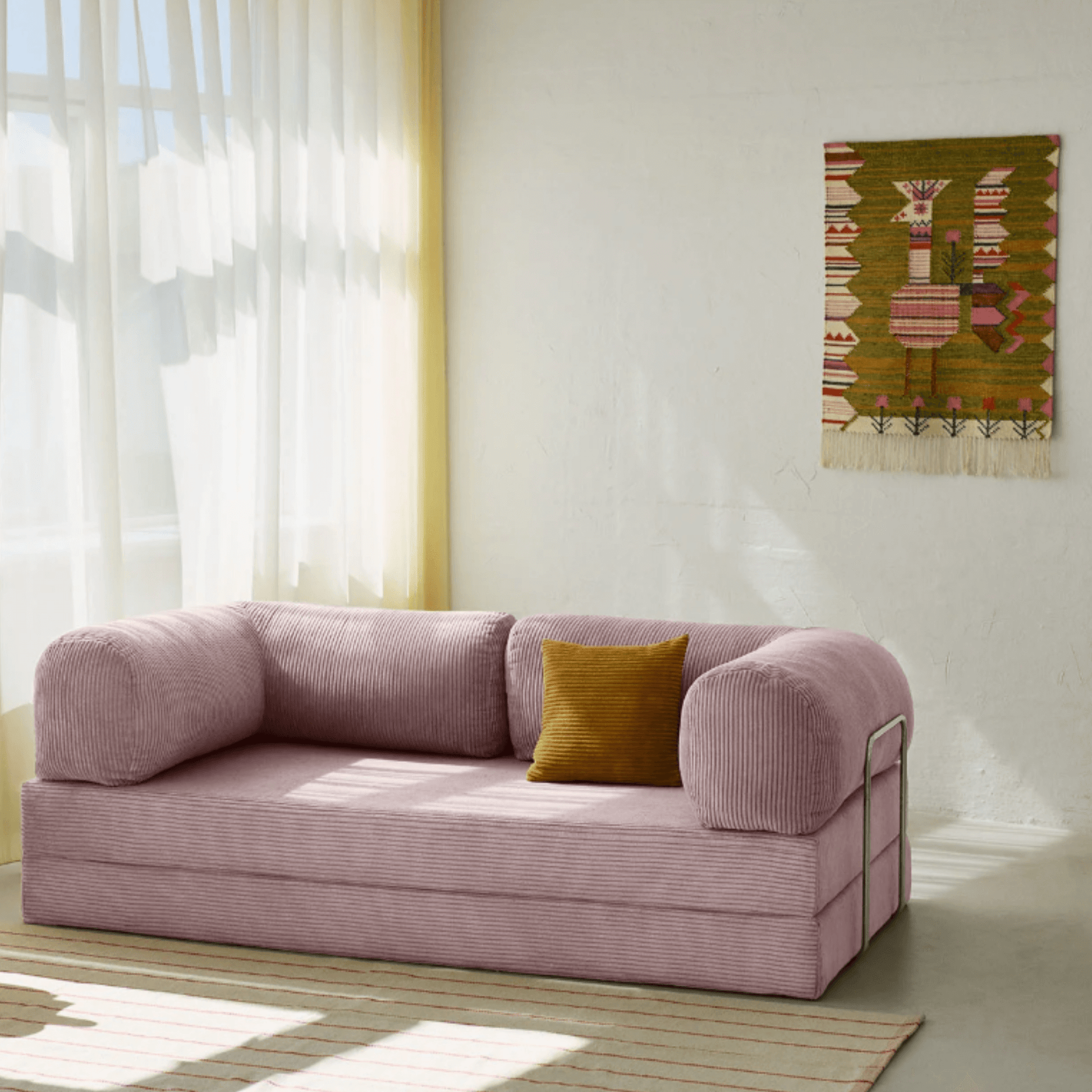 Primyhome pink corduroy convertible sofa bed in a sunlit living room with minimalist decor and boho wall art